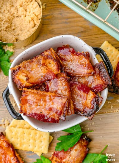 A bowl of candied bacon crackers with crackers and bacon sitting around it.