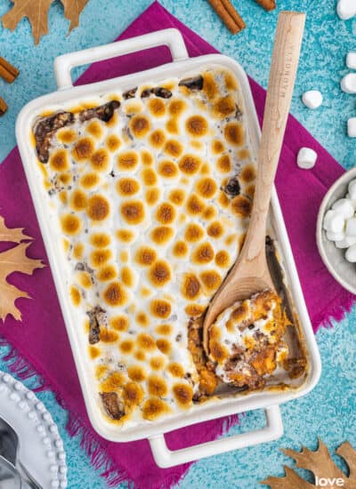A white casserole dish filled with candied yams topped with marshmallows.