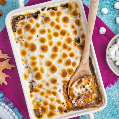 A white casserole dish filled with candied yams topped with marshmallows.