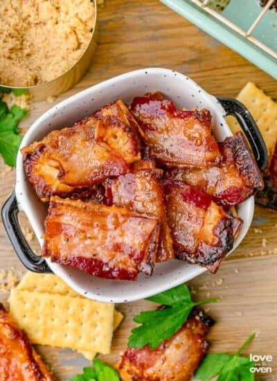 A bowl of candied bacon crackers with crackers and bacon sitting around it.