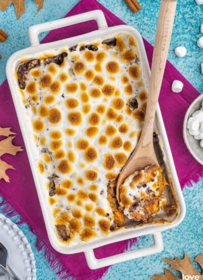 A white casserole dish filled with candied yams topped with marshmallows.