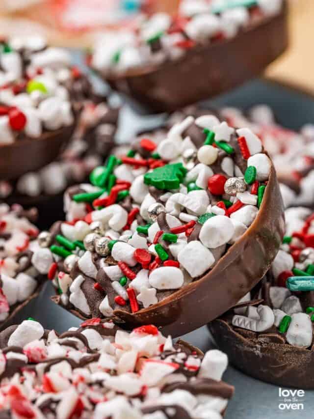 A variety of hot chocolate bomb cups laying together on a plate topped with Christmas sprinkles.