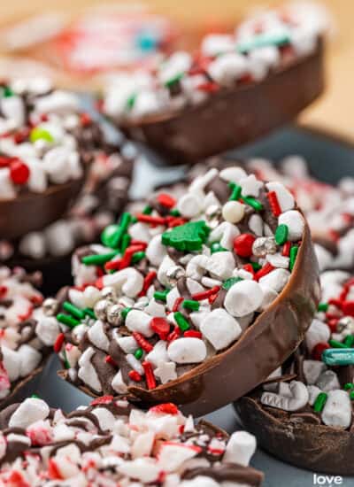 A variety of hot chocolate bomb cups laying together on a plate topped with Christmas sprinkles.