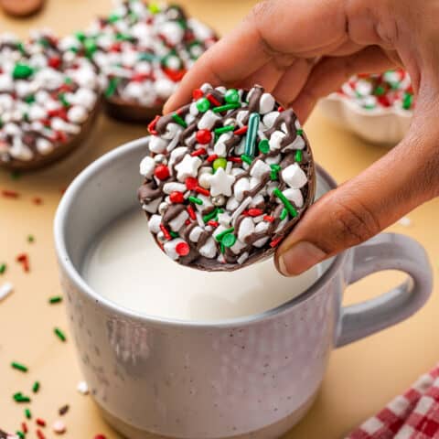 A hand dropping a hot chocolate bomb into a mug of milk.