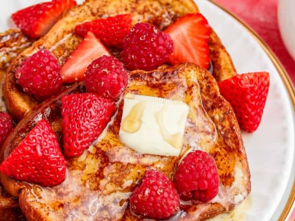 A plate of french toast topped with syrup and strawberries.