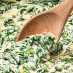 Creamed spinach in a pan with a wooden spoon