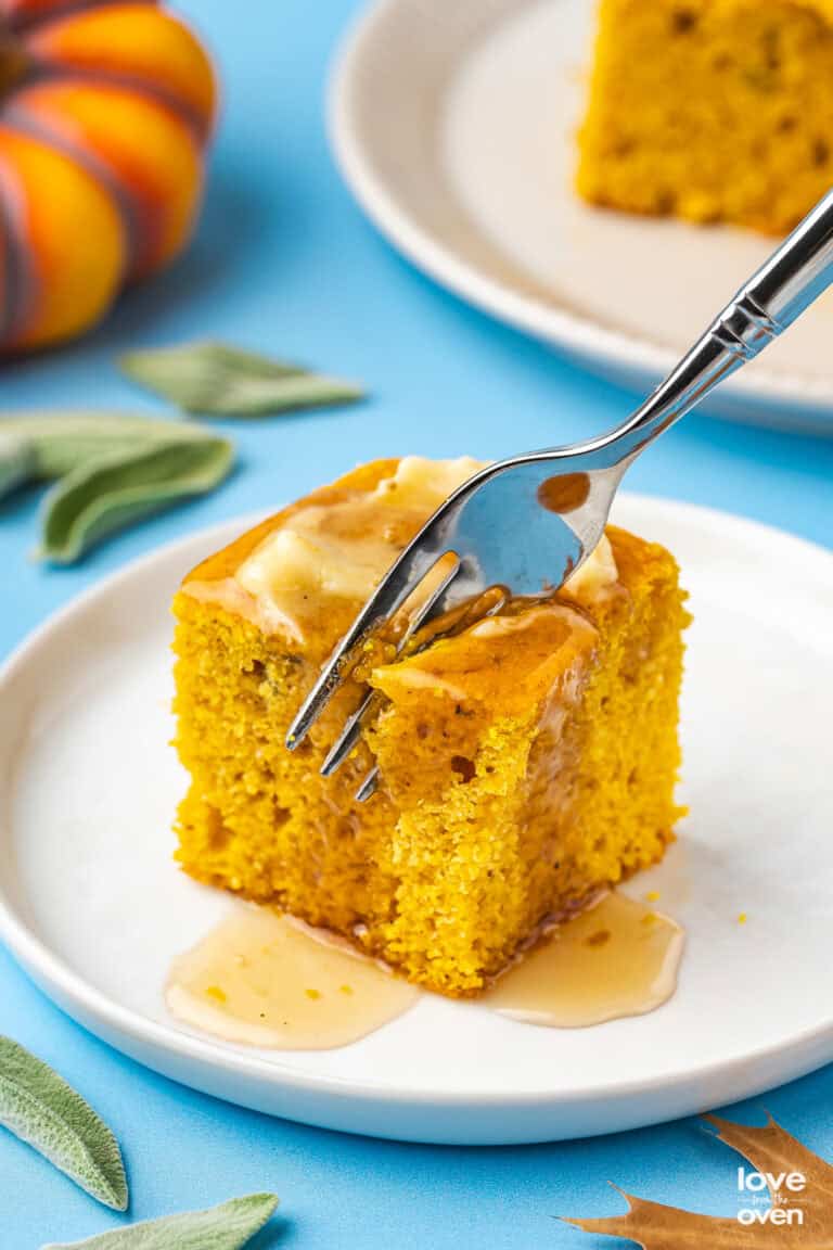 A fork cutting into a piece of pumpkin cornbread with butter on top