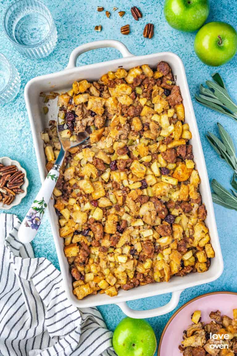 An overhead photo of a white casserole dish containing sausage apple stuffing and a spoon