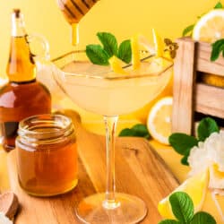 a glass with a bees knees cocktail in it and honey being drizzled in