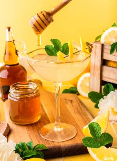 a glass with a bees knees cocktail in it and honey being drizzled in