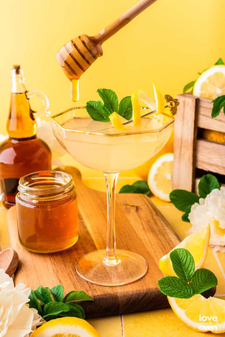 a glass with a bees knees cocktail in it and honey being drizzled in