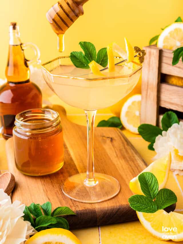 a glass with a bees knees cocktail in it and honey being drizzled in