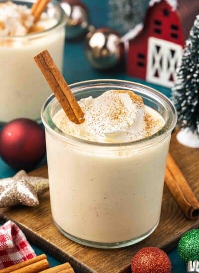 A glass of eggnog with whipped cream and a cinnamon stick