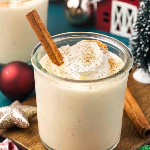 A glass of eggnog with whipped cream and a cinnamon stick
