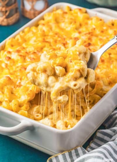 A spoon taking a scoop of Tinis Mac and Cheese out of a white casserole dish