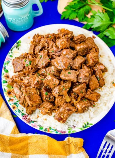 A plate of crockpot steak bites on a blue background