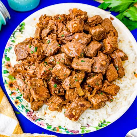 A plate of crockpot steak bites on a blue background