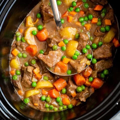 A black crockpot full of beef stew with vegetables
