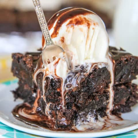 A brownie topped with melting vanilla ice cream with a fork taking a piece.