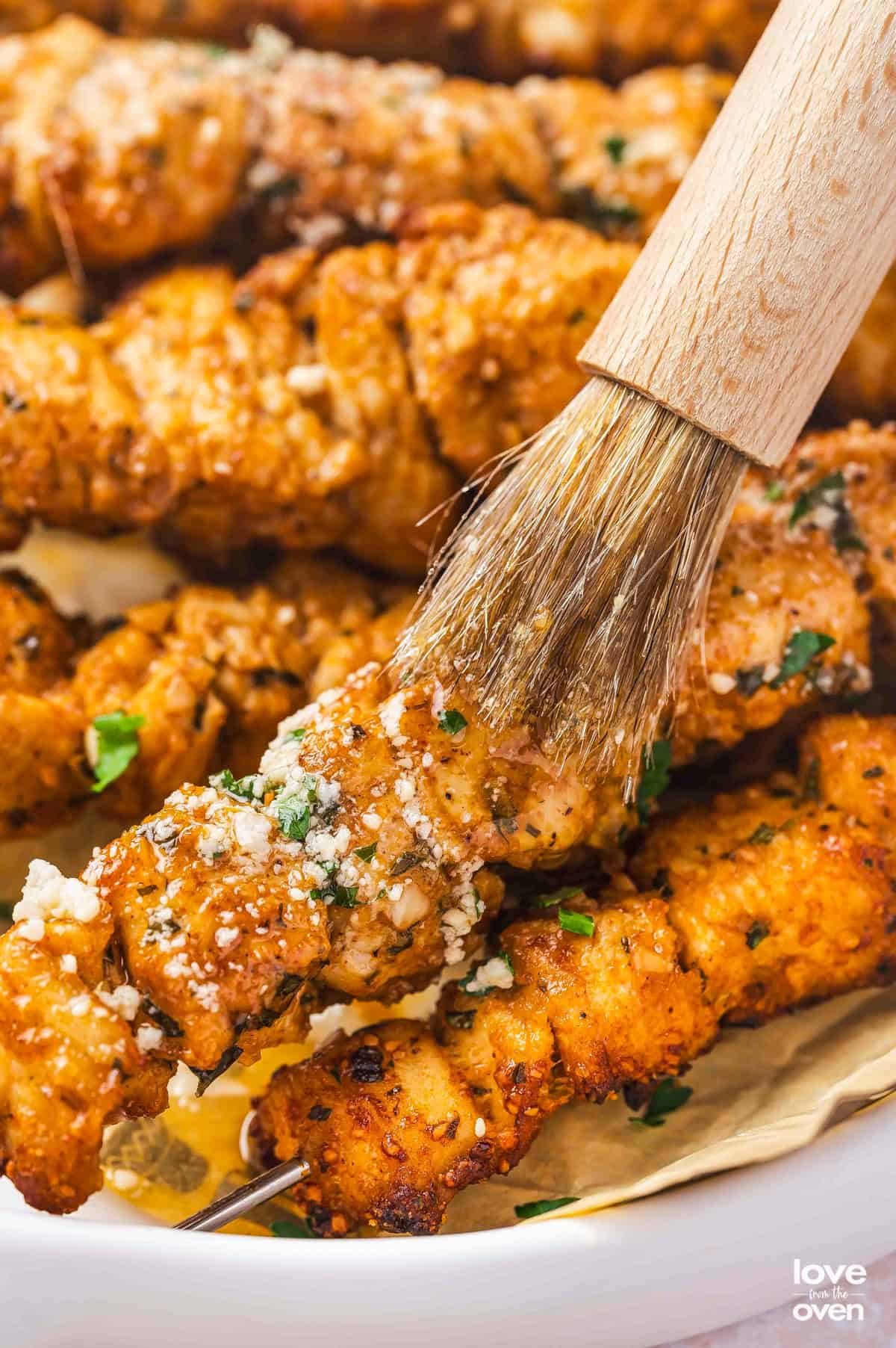 A brush adding garlic butter sauce to chicken skewers