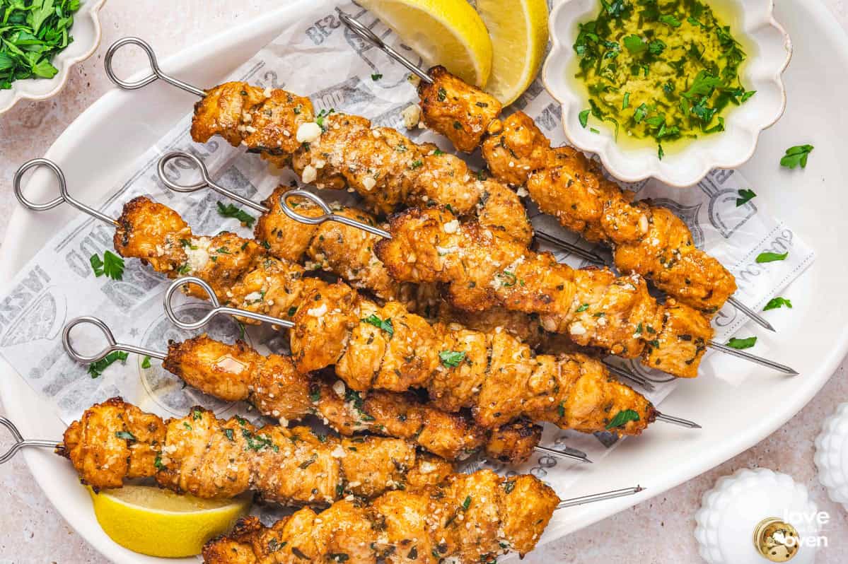 A plate of chicken skewers with a garlic butter sauce and lemons