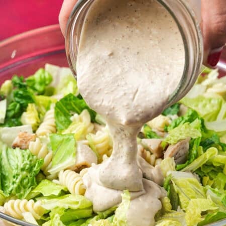 Caesar Dressing being poured from a jar onto a salad.