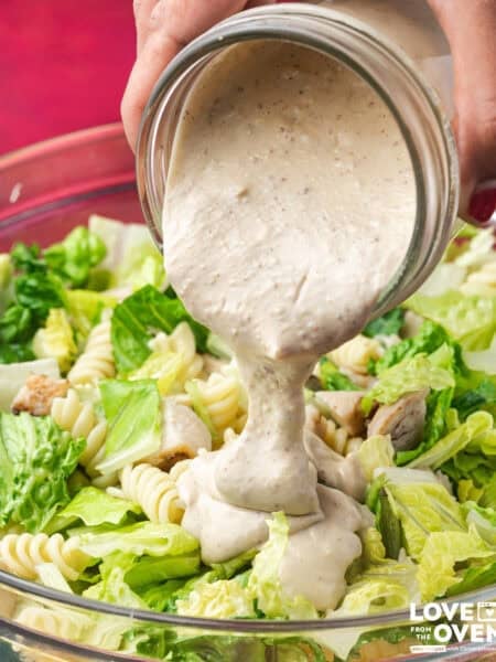 Caesar Dressing being poured from a jar onto a salad.