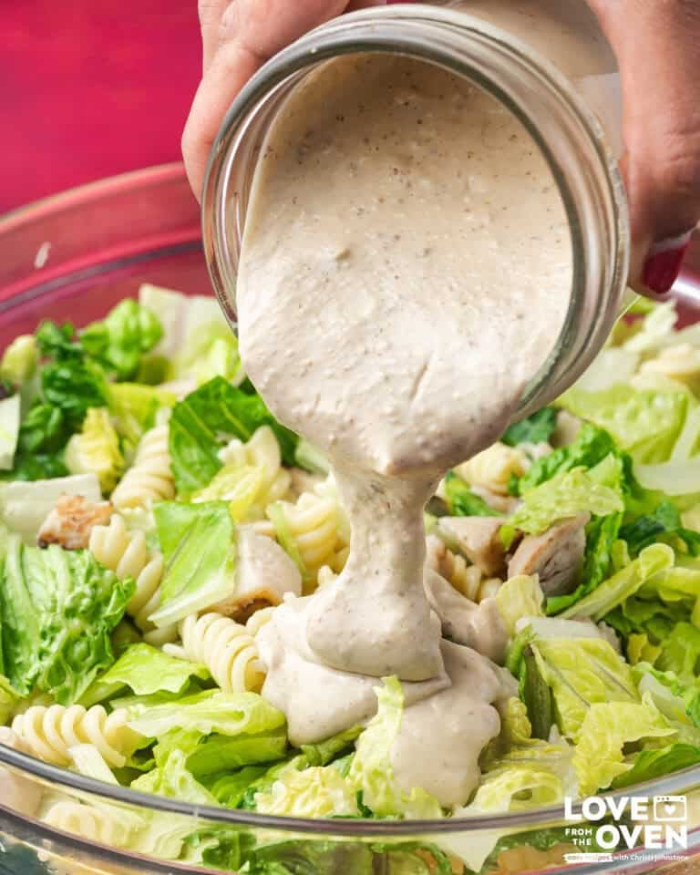 Caesar Dressing being poured from a jar onto a salad.