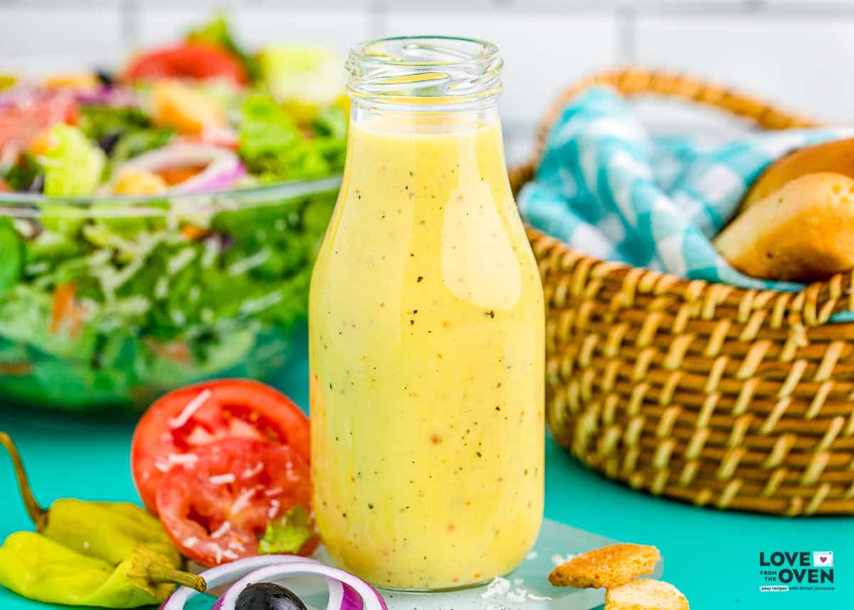A bottle of salad dressing with breadsticks and salad behind it