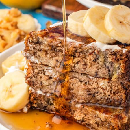 Slices of banana bread French toast stacked on top of each other with syrup being poured