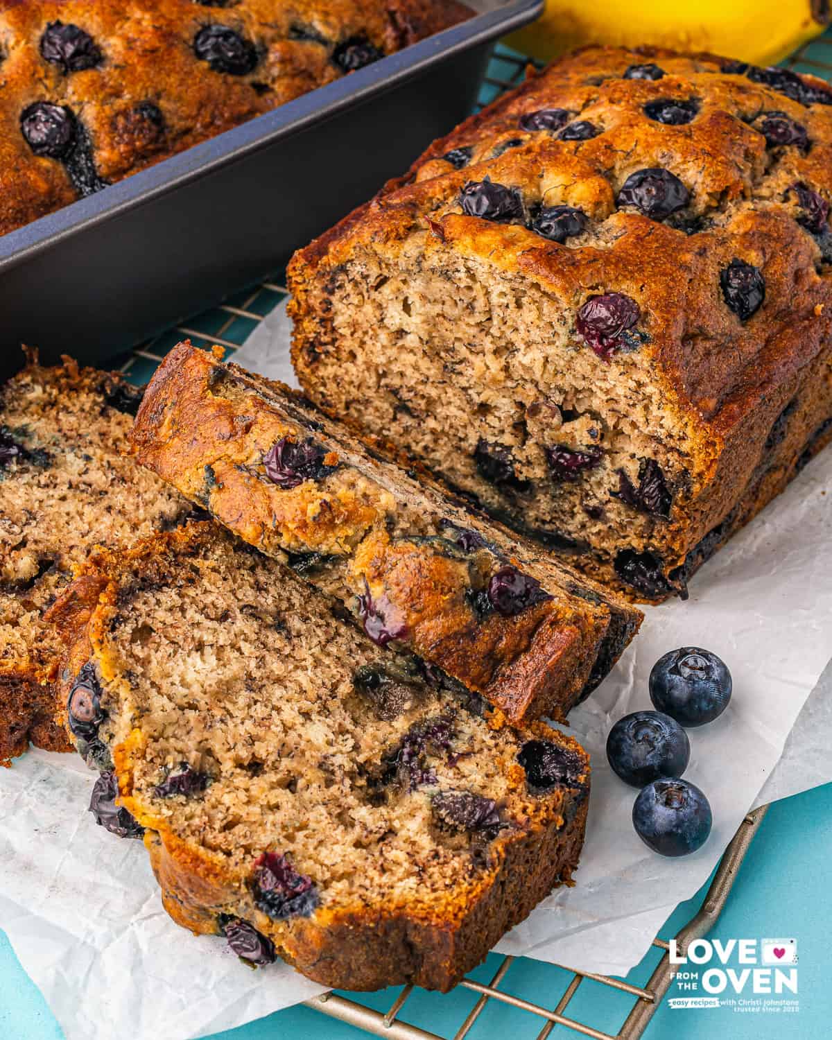 A loaf of blueberry banana bread wit slices cut and loose blueberries next to it.