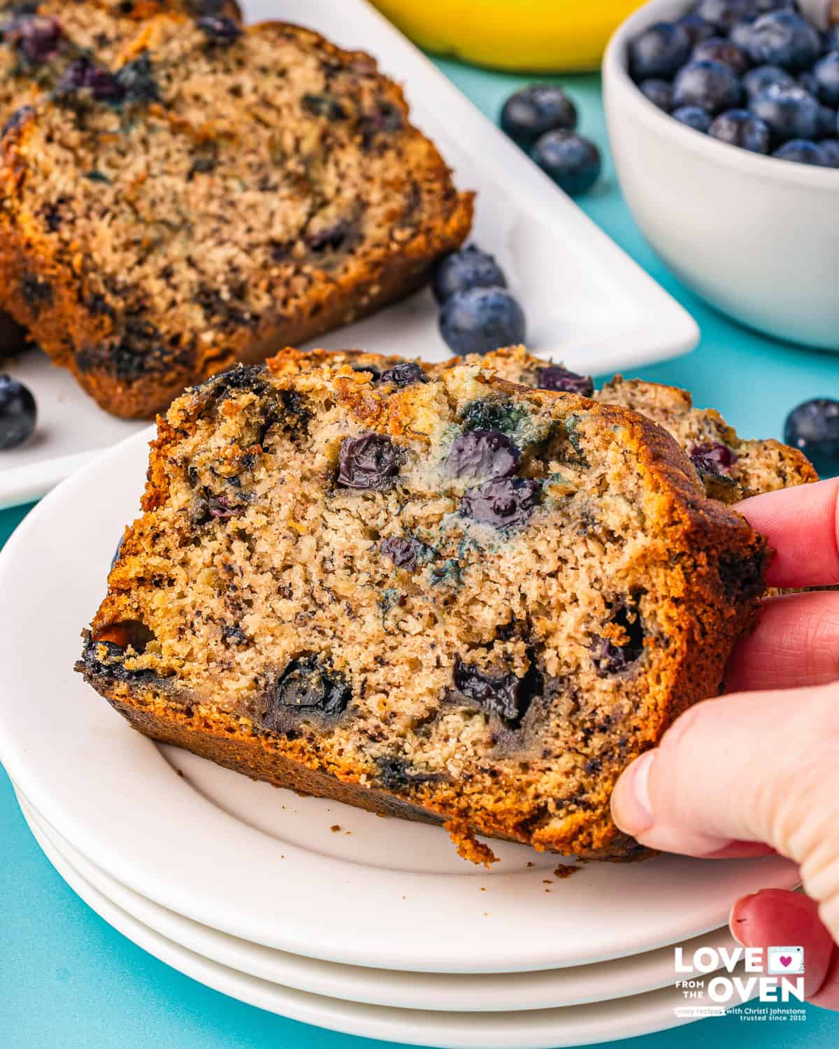 A hand grabbing a slice of bluerberry banana bread